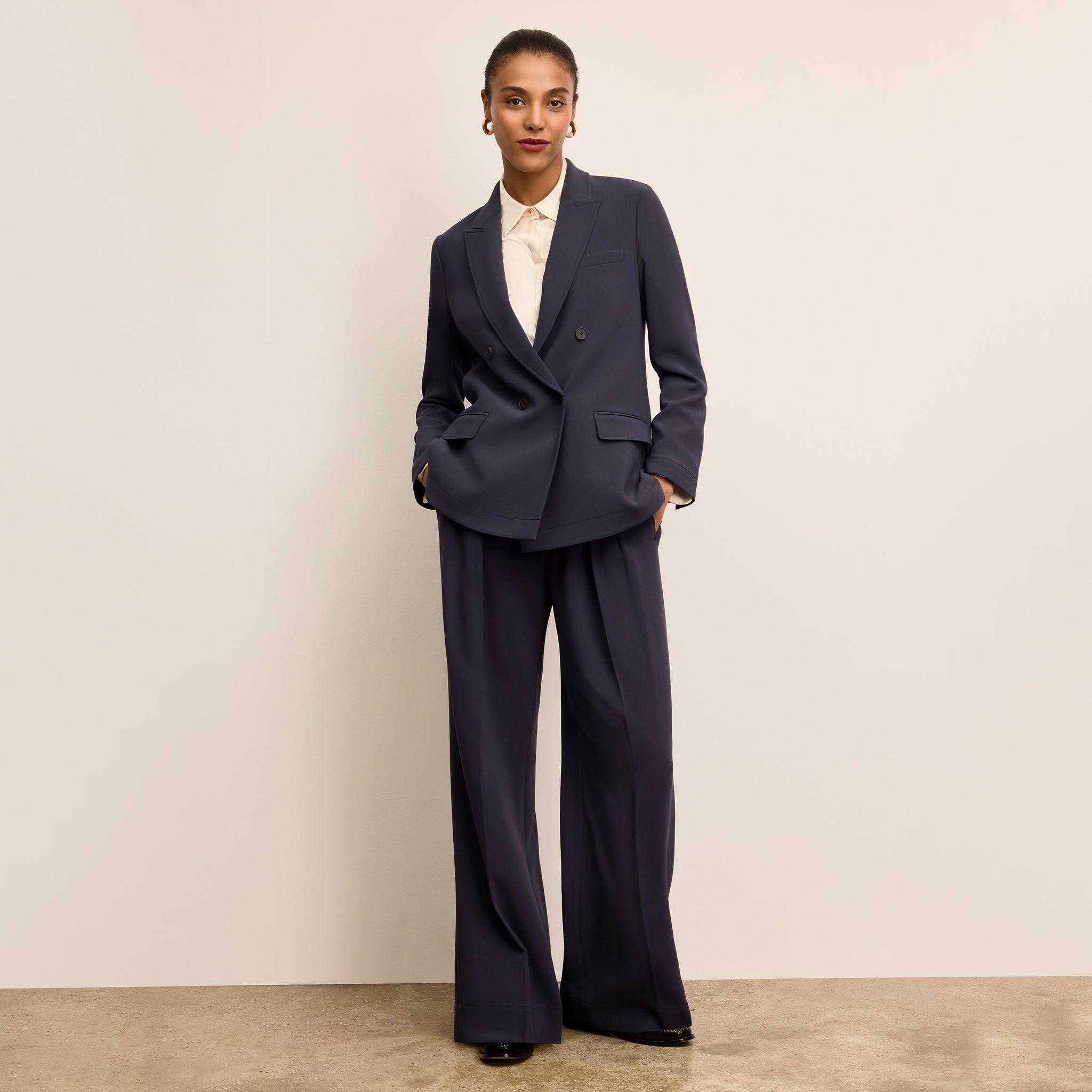 Woman wearing a navy suit with a white shirt against a beige background