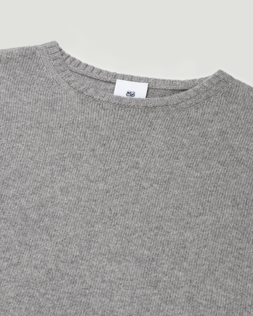 Close-up of a gray sweater with a brand label on a light gray background.