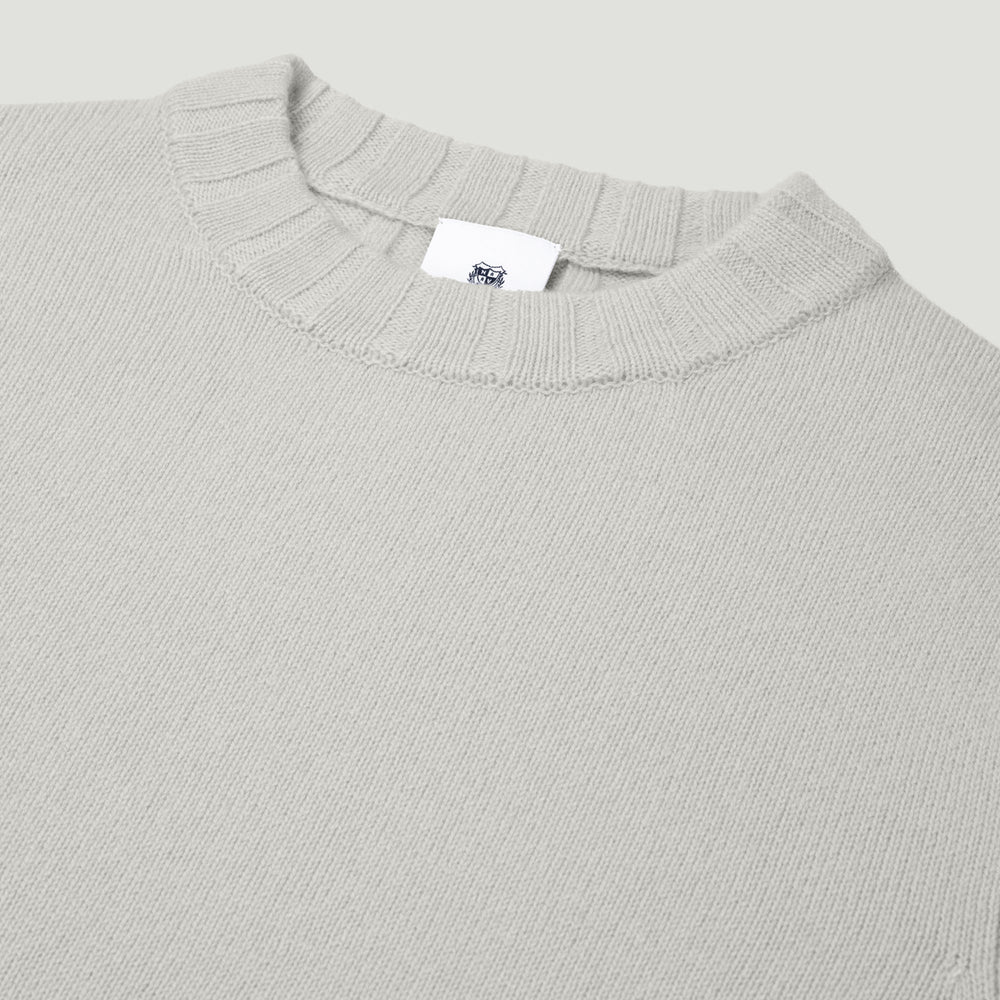 Close-up of a gray ribbed sweater with a brand label on a light gray background