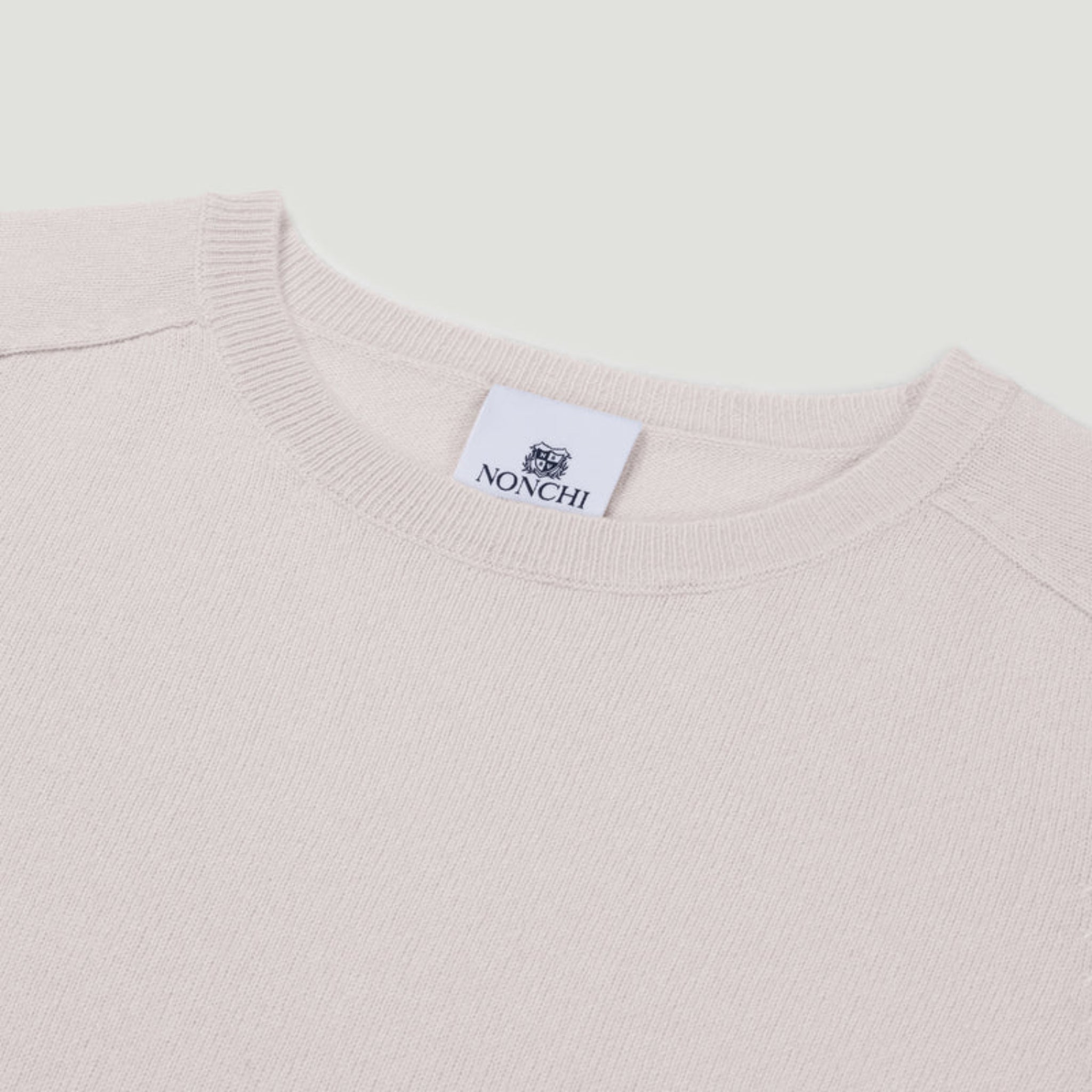 Close-up of a light pink sweater with a Nonchi label on a white background