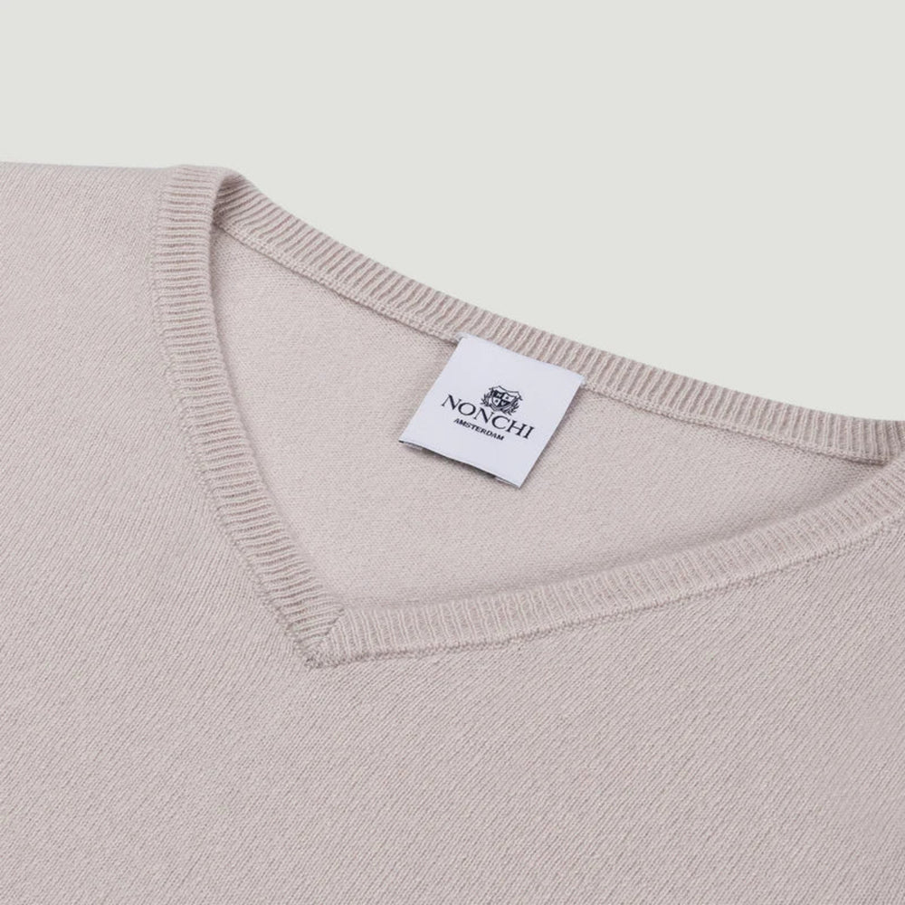 Close-up of a beige sweater with a brand label on a light gray background