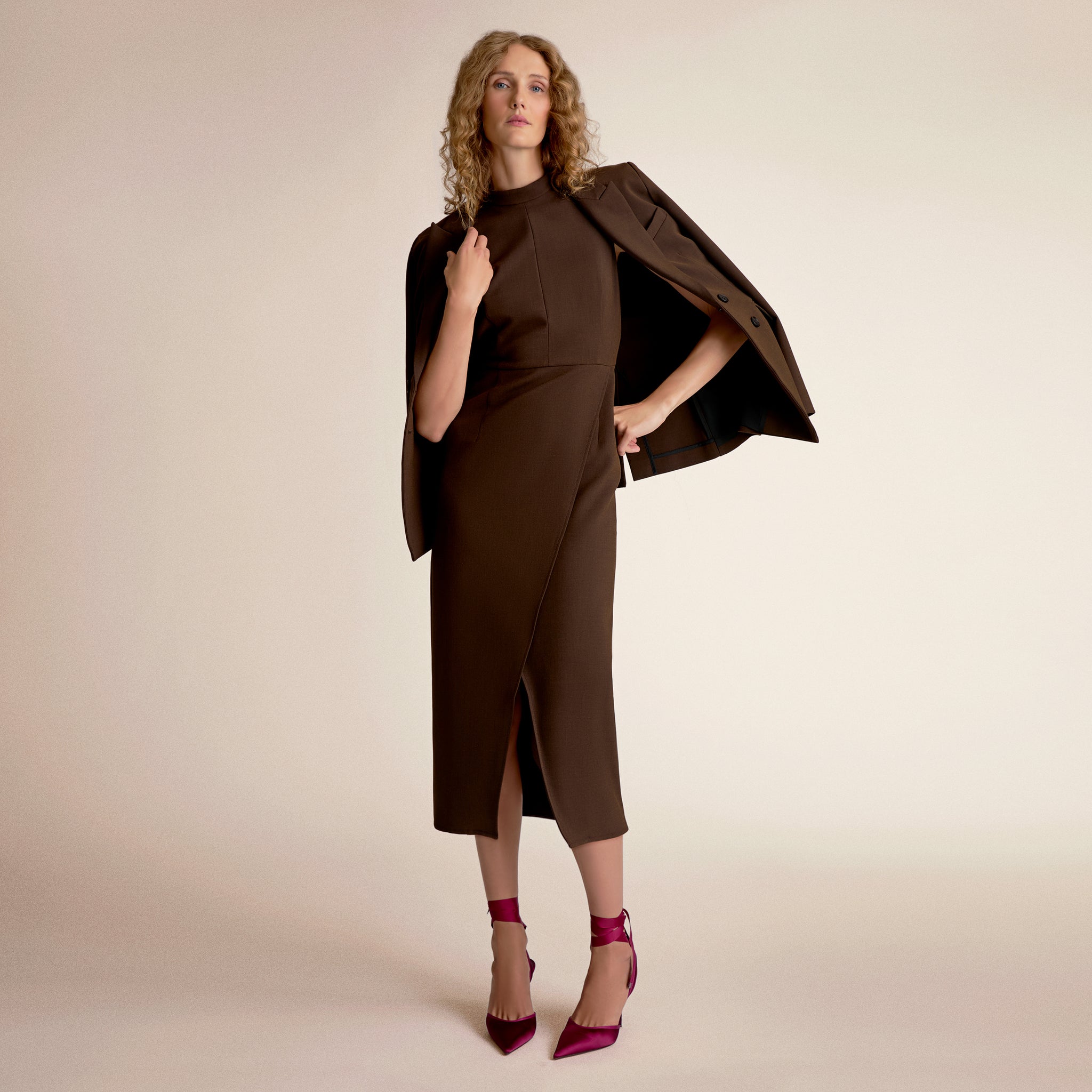 Woman wearing a brown dress with a matching jacket against a beige background