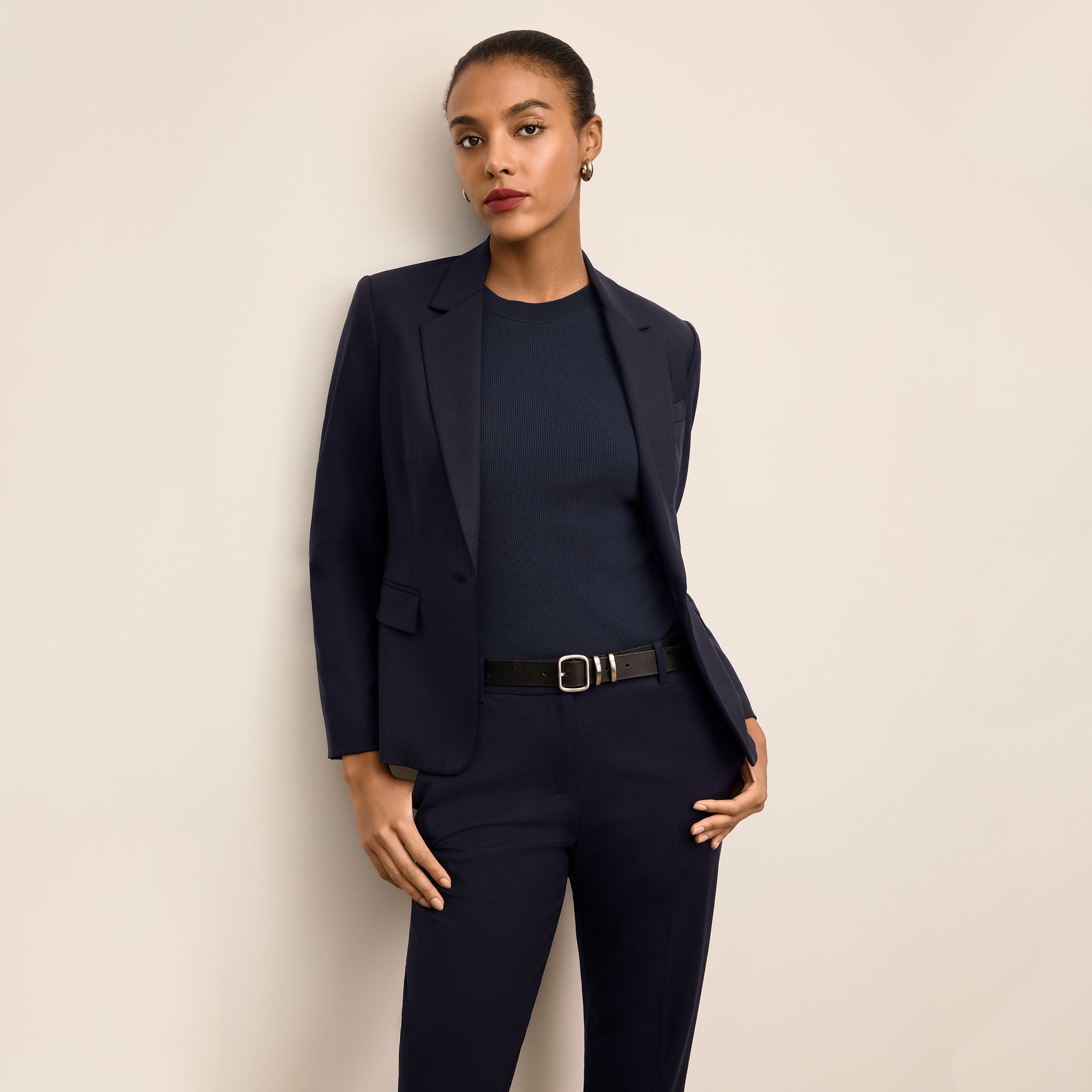 Woman wearing a navy suit with a belt against a beige background