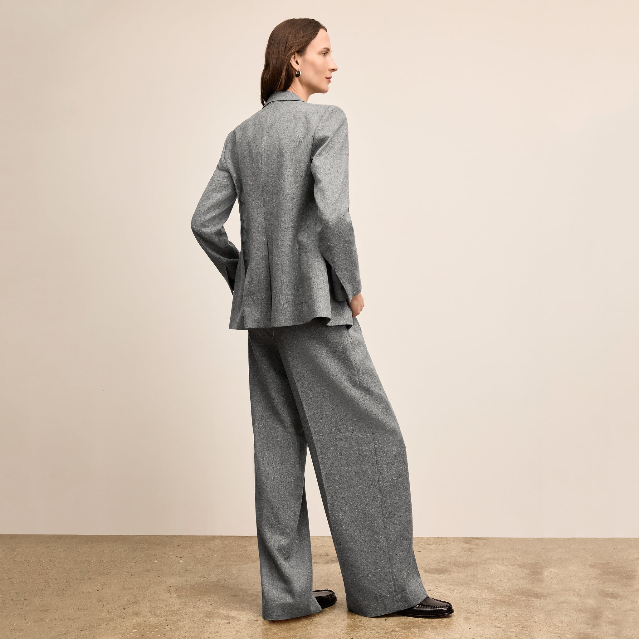 Woman wearing a gray suit standing against a beige background
