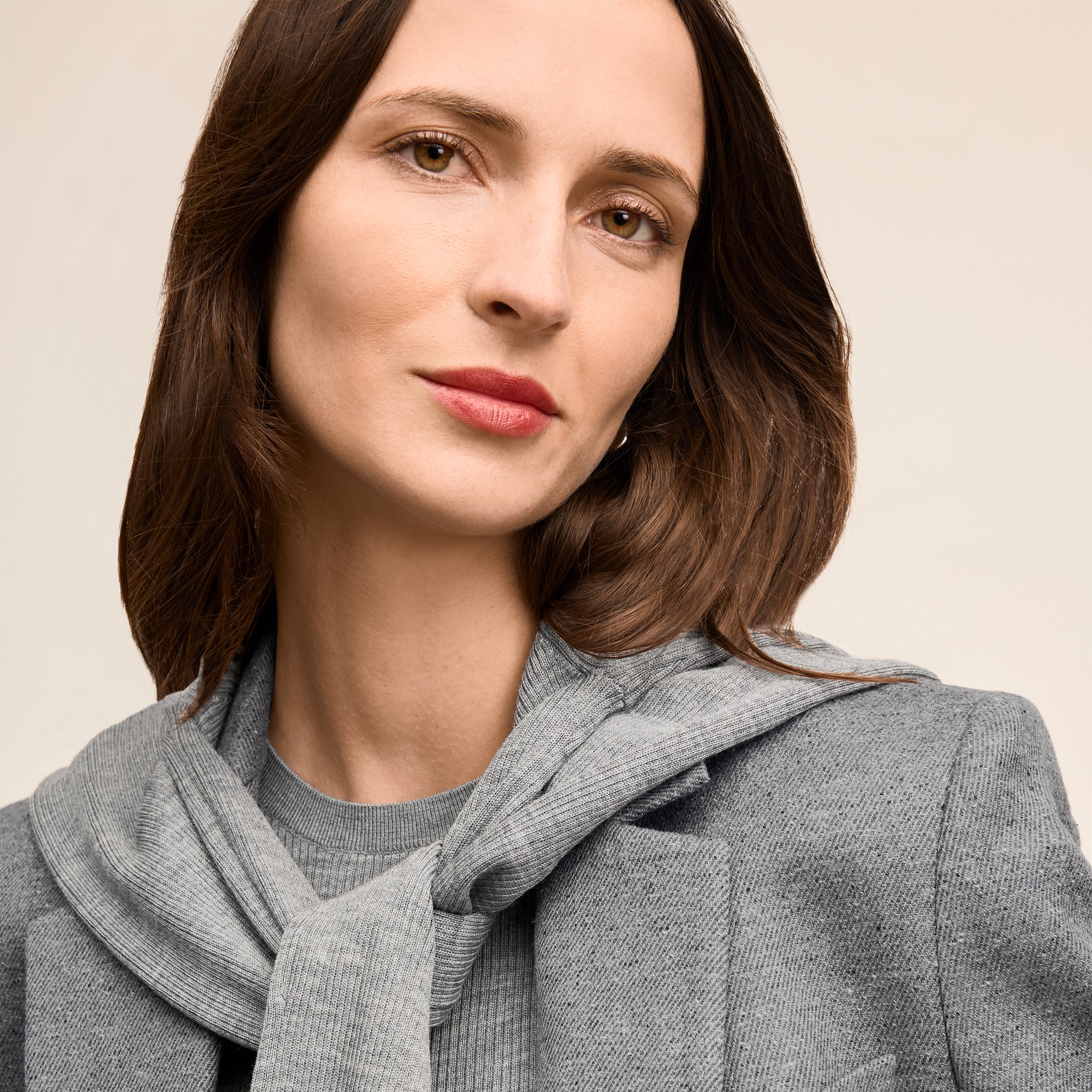 Woman wearing a gray scarf and coat against a beige background