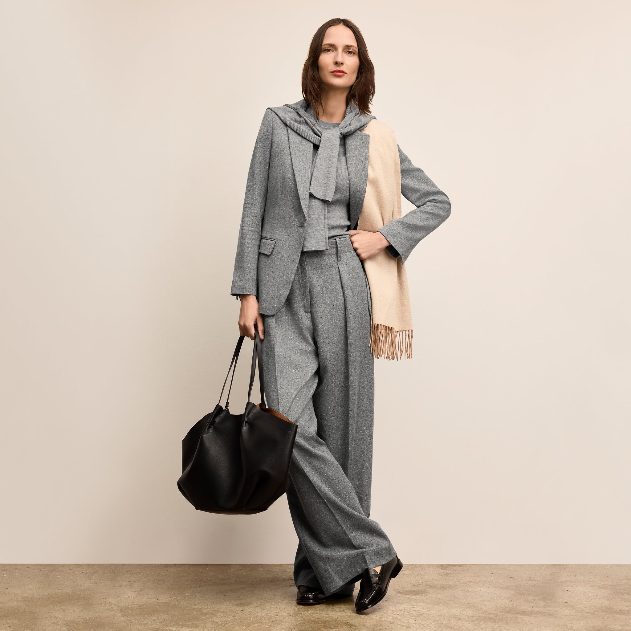 Woman in a gray suit with a beige scarf and black bag against a beige background