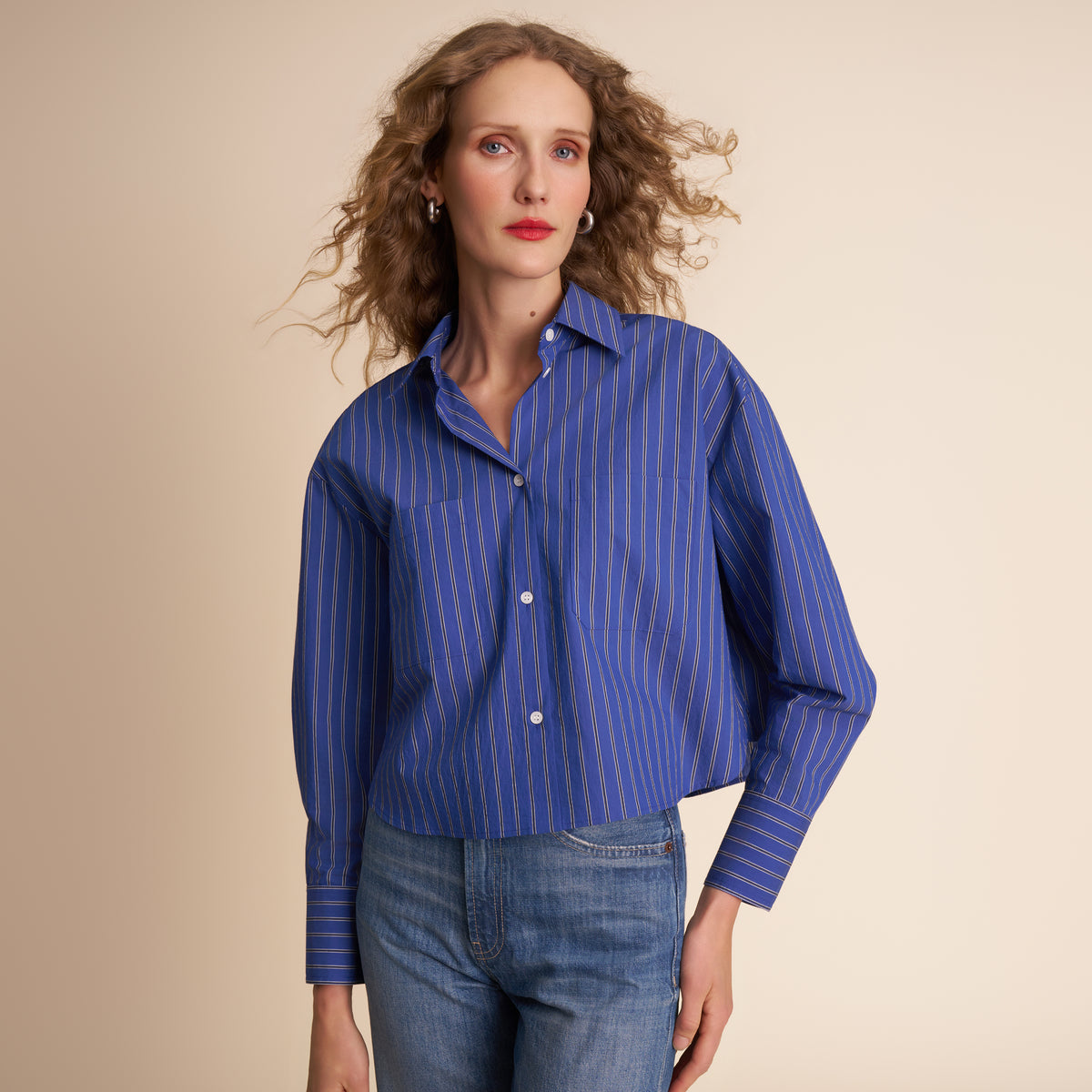 Woman wearing a blue striped shirt and jeans against a beige background