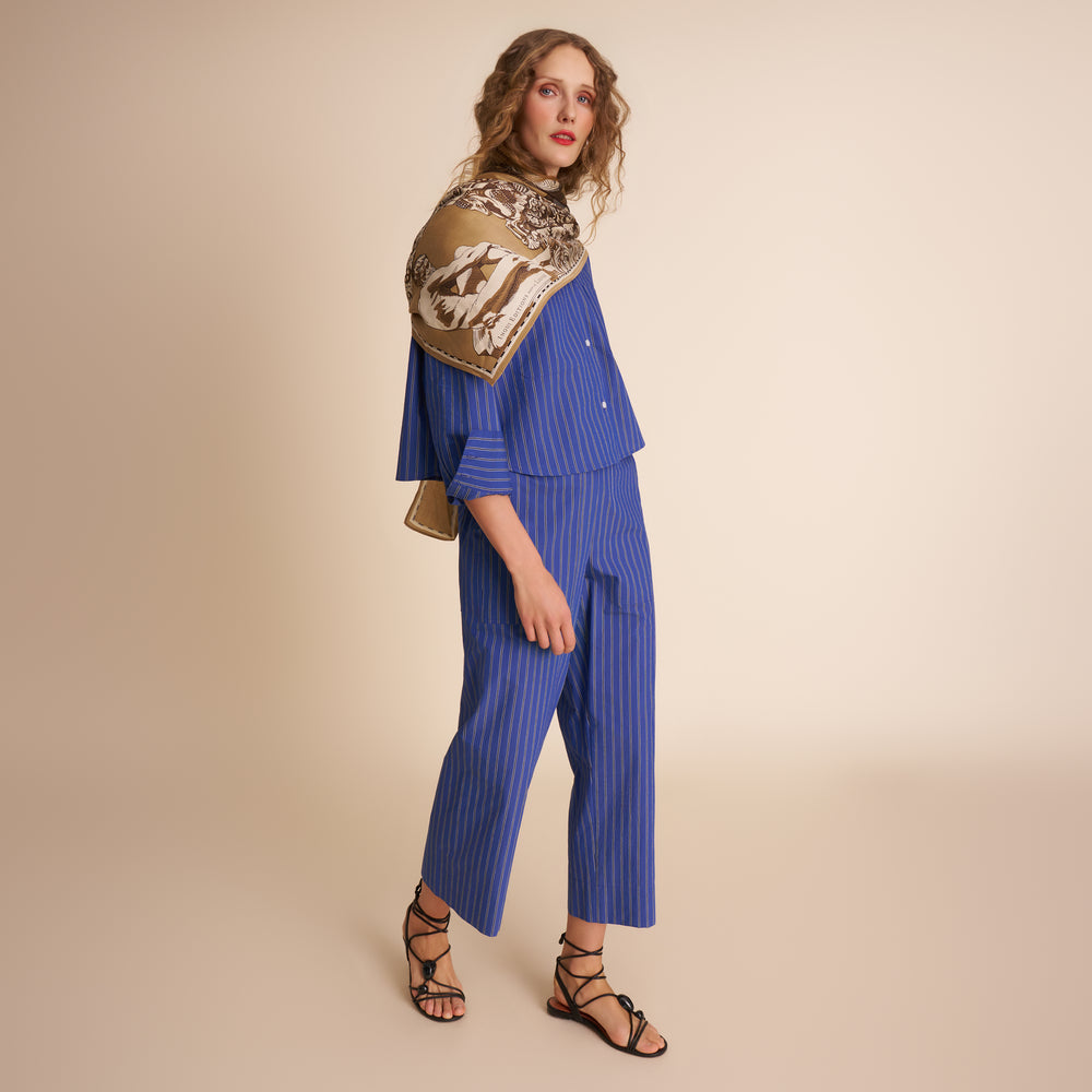 Woman wearing a blue outfit with a patterned scarf on a beige background
