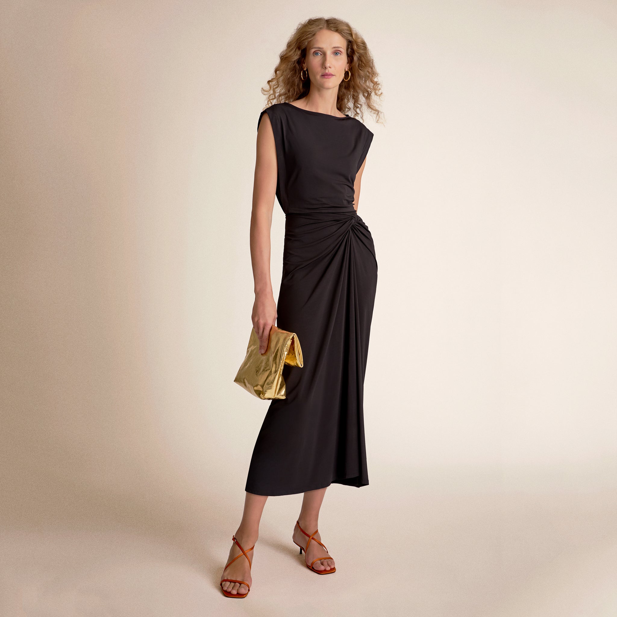 Woman wearing a black dress holding a gold clutch 