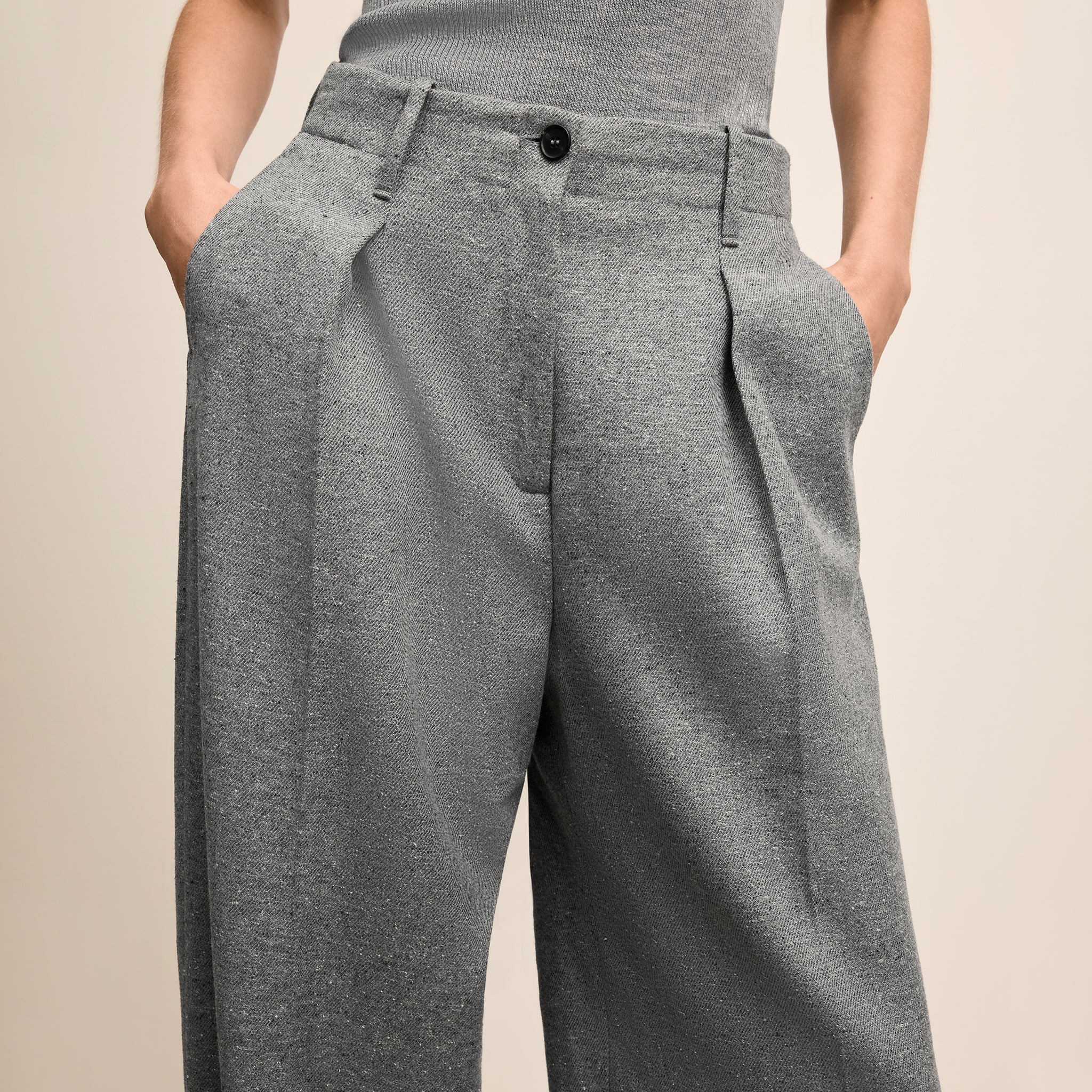 Gray pleated pants worn by a person on a beige background