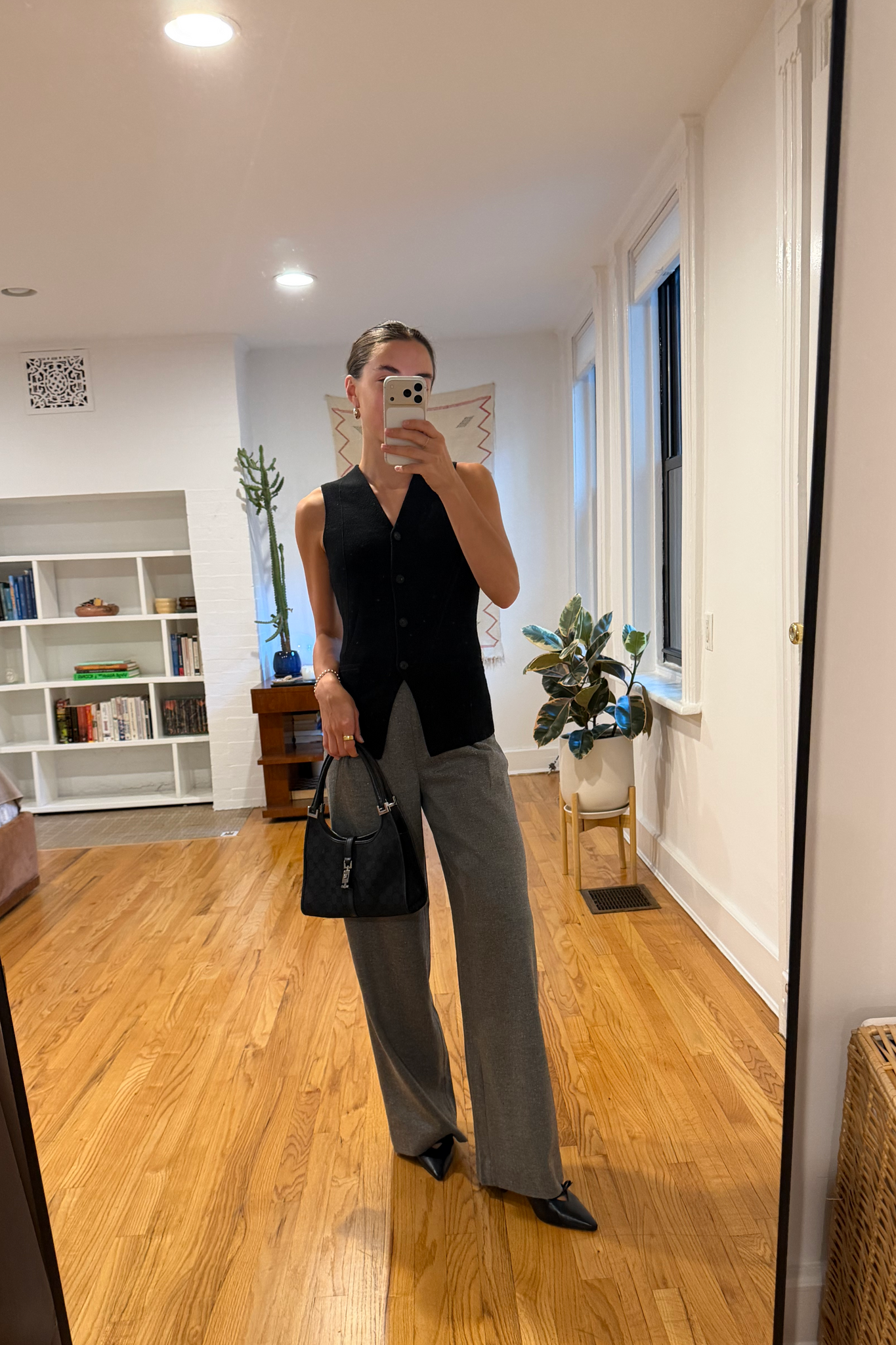 Person taking a mirror selfie in a room with wooden flooring and white walls.