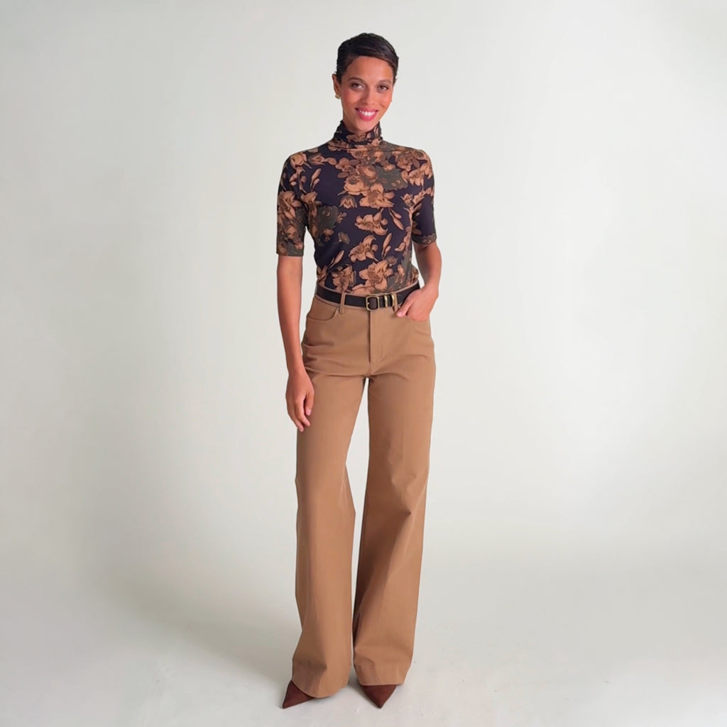 Video of a woman wearing a fitted short-sleeve mock-neck top with a dark floral print in beige and brown tones, 