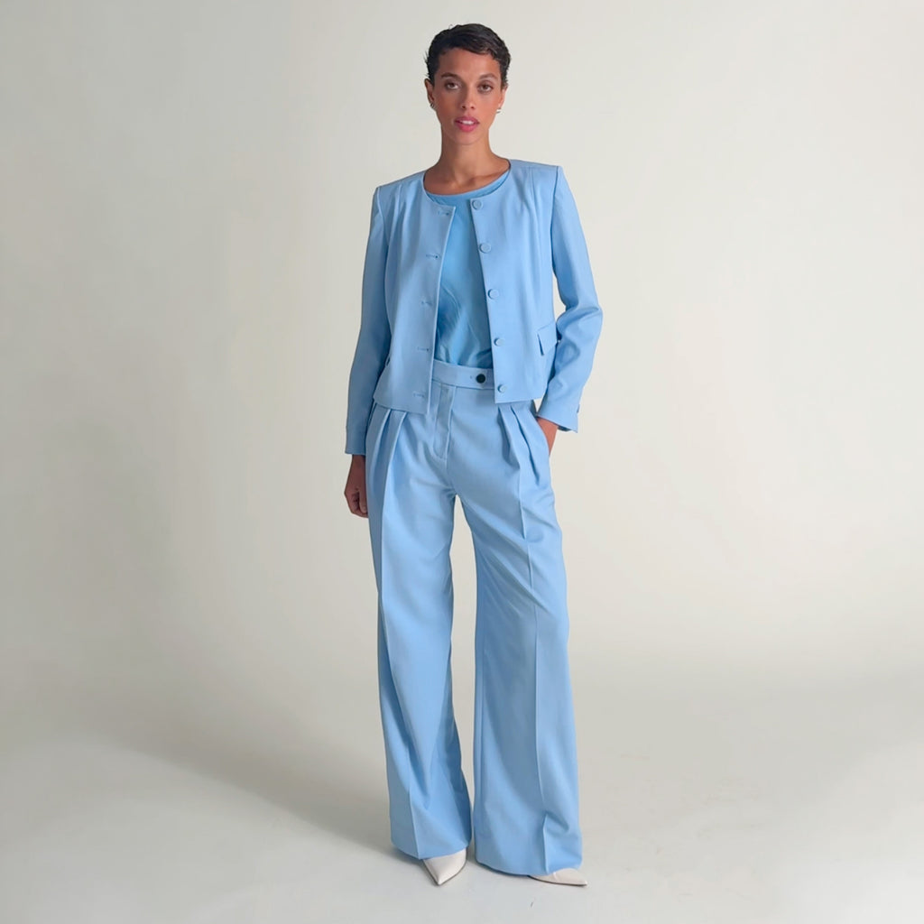 Video of a woman wearing a light blue pant and blazer and floral top on a beige background