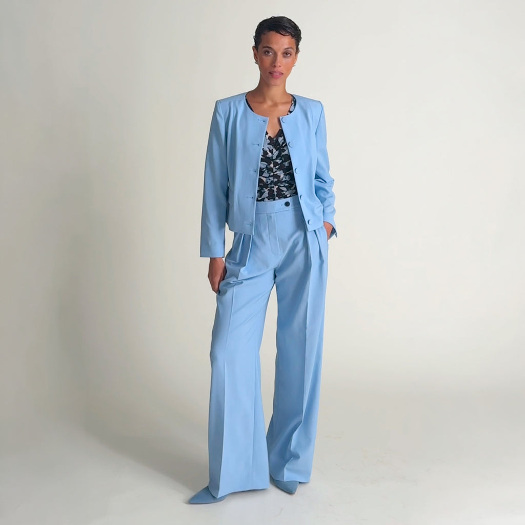 Video of a woman wearing a light blue pant and floral top on a beige background |