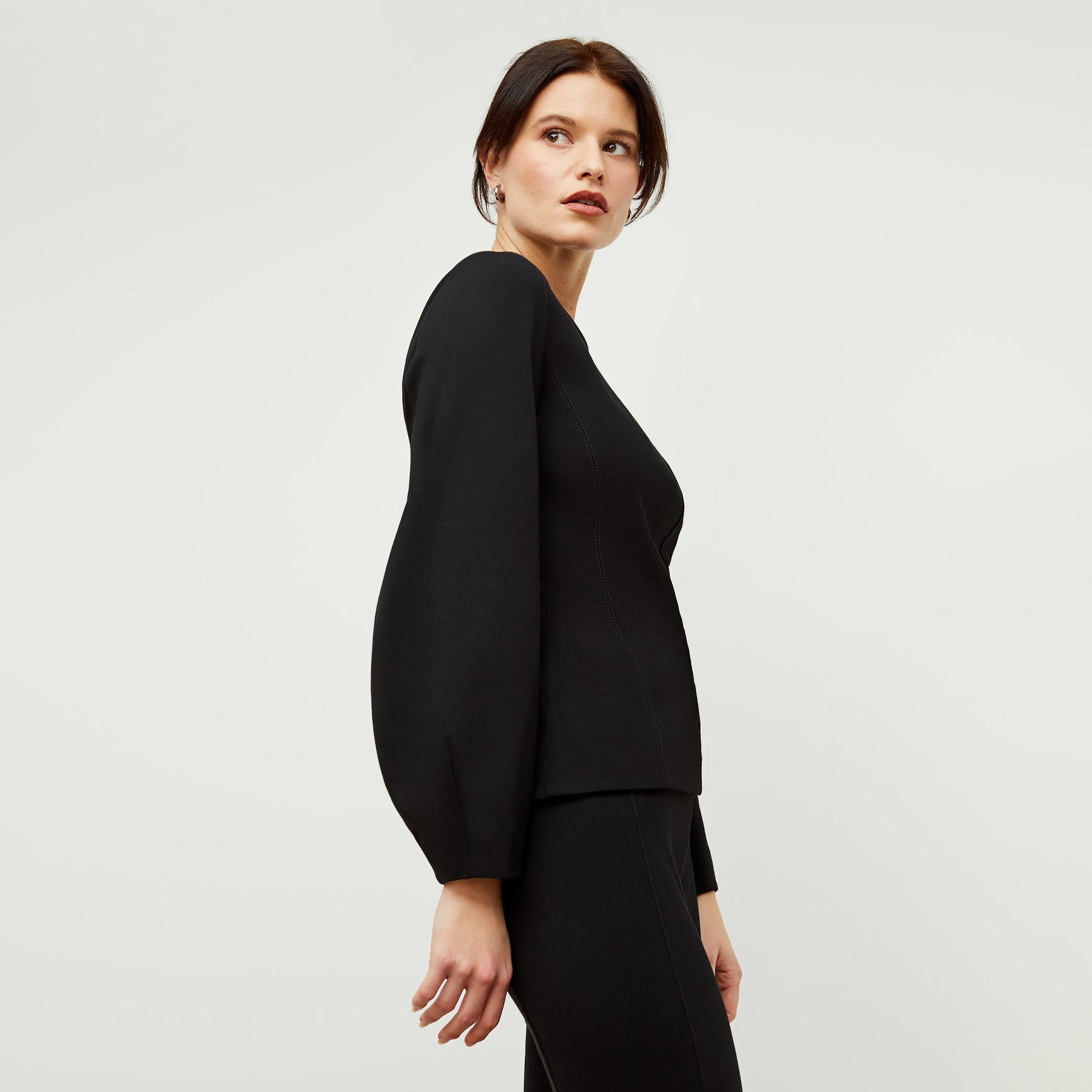 Side image of a woman standing wearing the rashida top in black