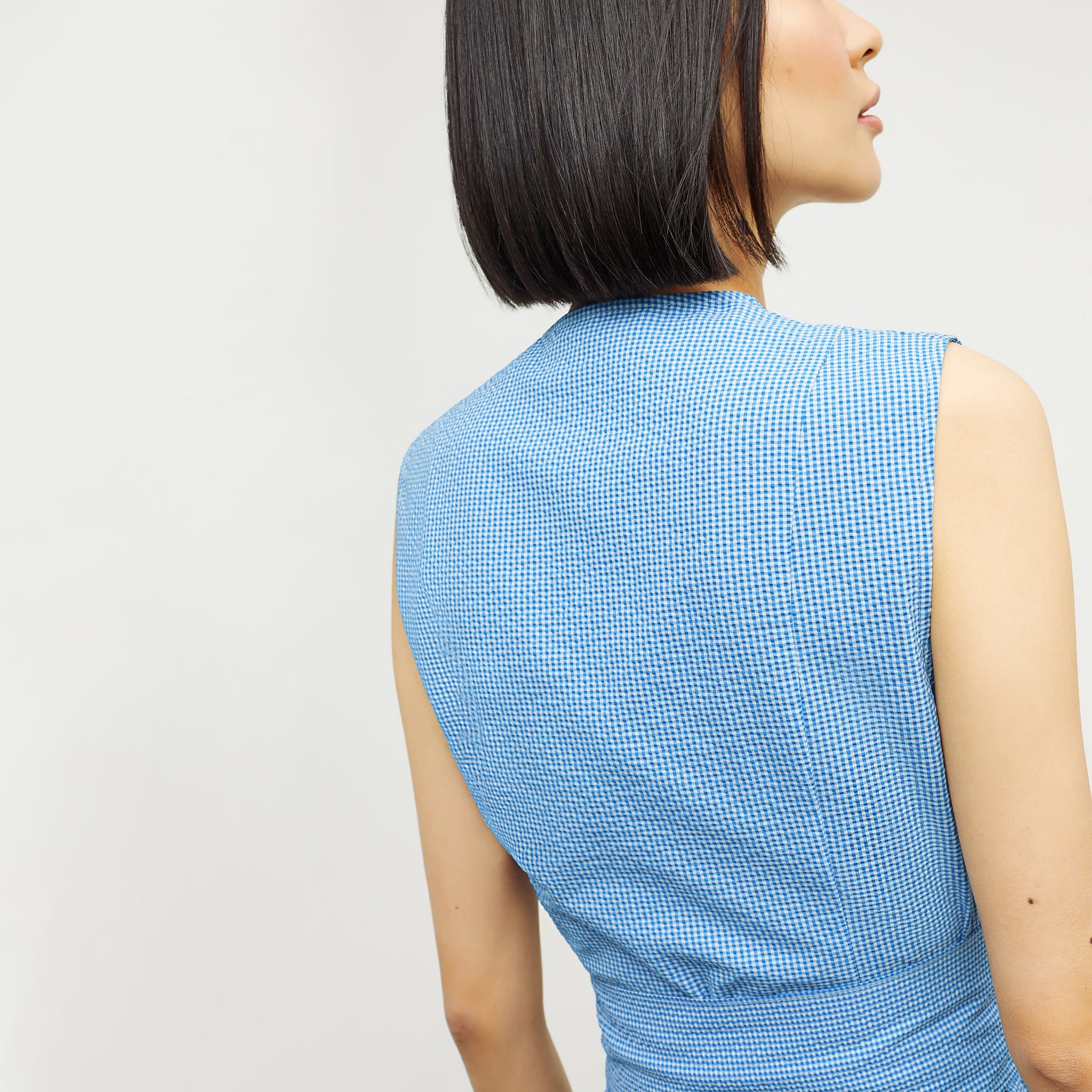 Back image of a woman standing wearing the ellen top in gingham seersucker in capri blue and white