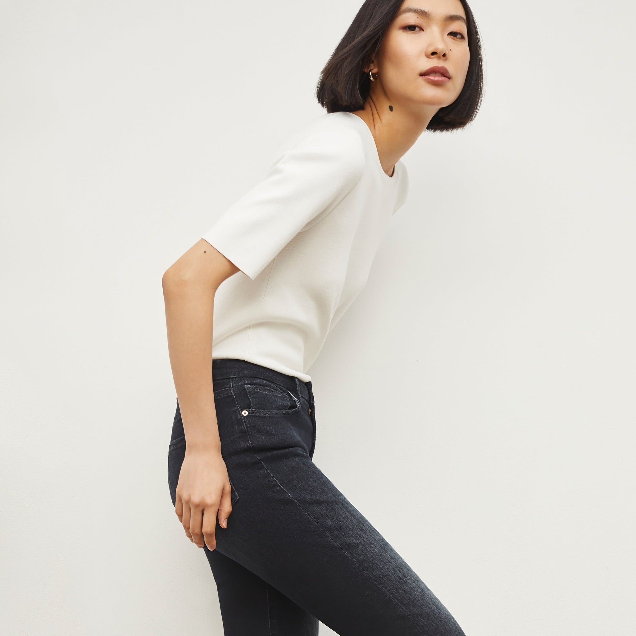 Side image of a woman standing wearing the FRAME Denim Le Crop Slim Bootcut Raw Edge Jean in Marcella