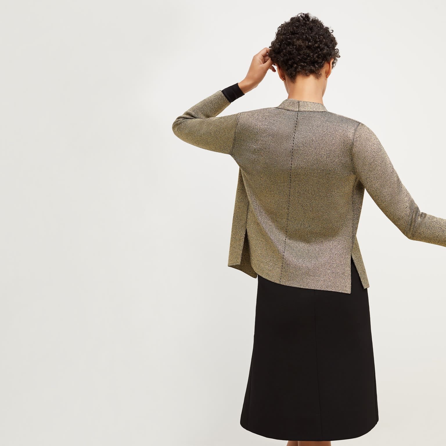 Back image of a woman standing wearing the Woolf Jardigan—Gold Knit in Black / Gold