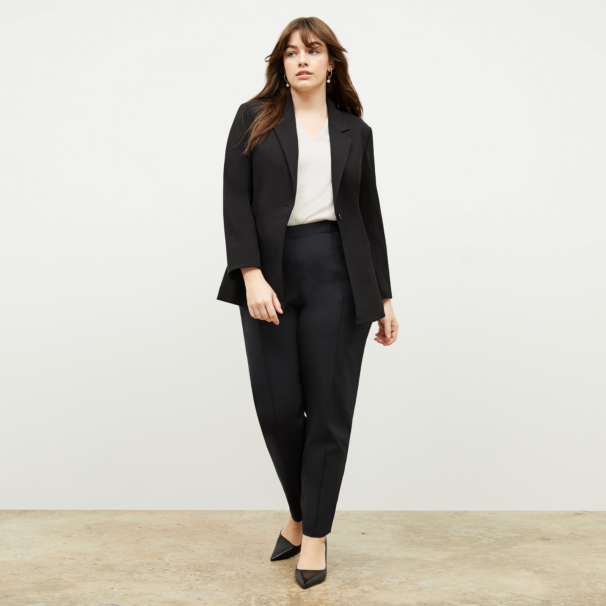 Front image of a woman standing wearing the moreland jacket--origami suiting in black