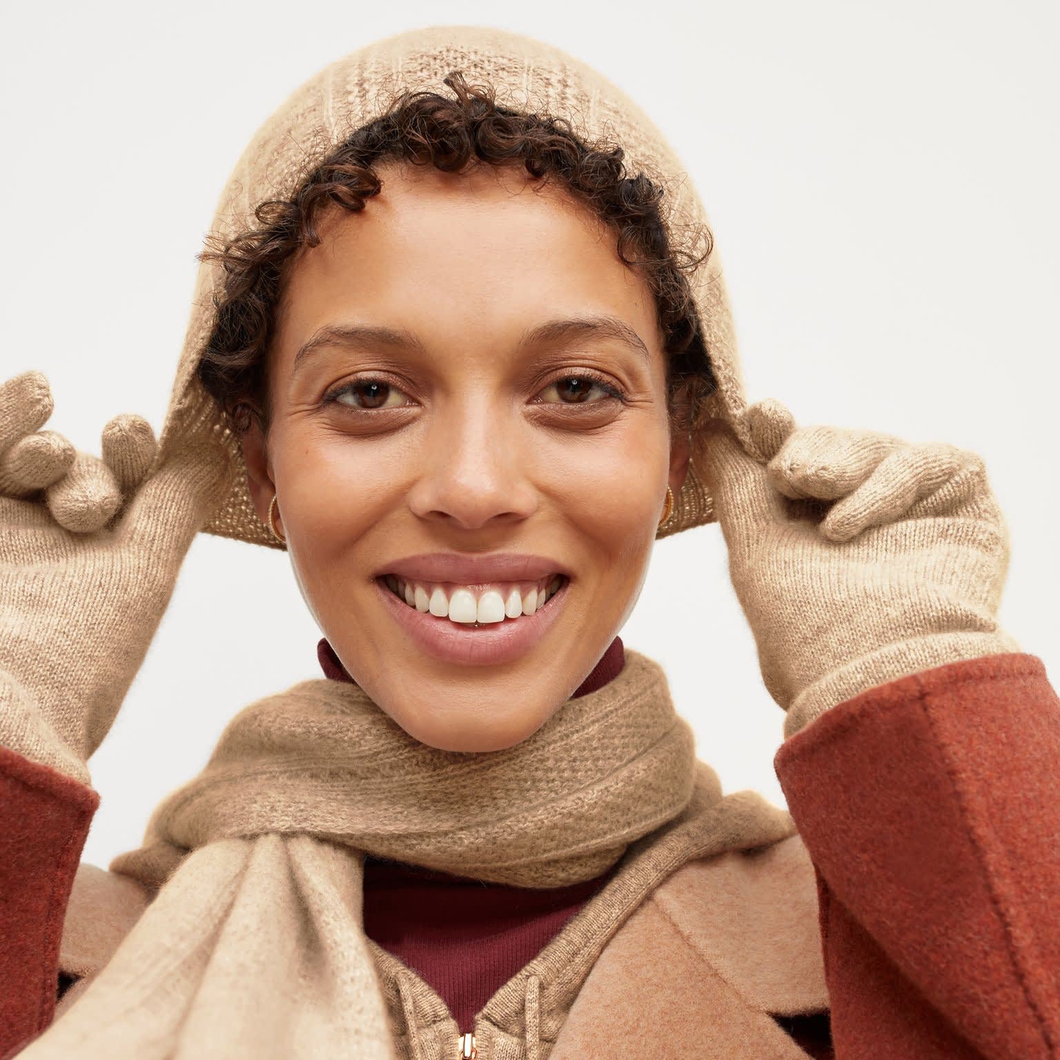 Front image of a woman standing wearing the Circle Cable Beanie—Cashmere in Light Camel
