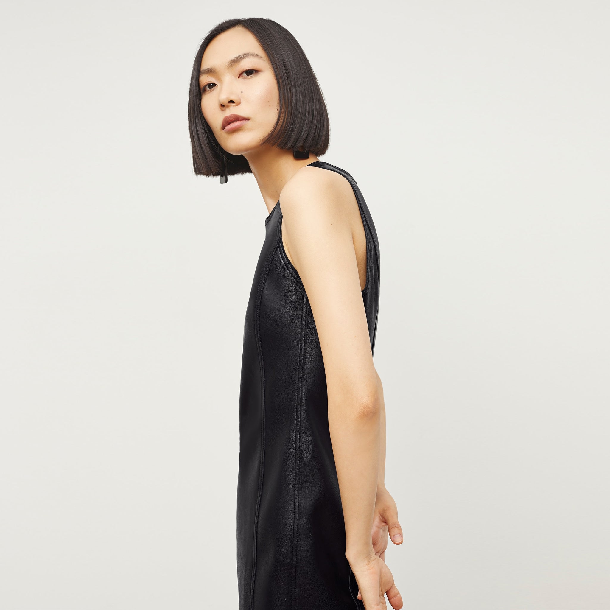 Side image of a woman standing wearing the Chloe Dress—Vegan Leather in Black