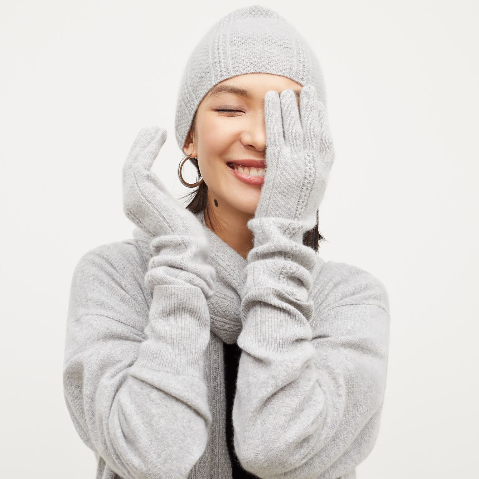 Front image of a woman standing wearing the Circle Cable Beanie—Cashmere in Heather Gray