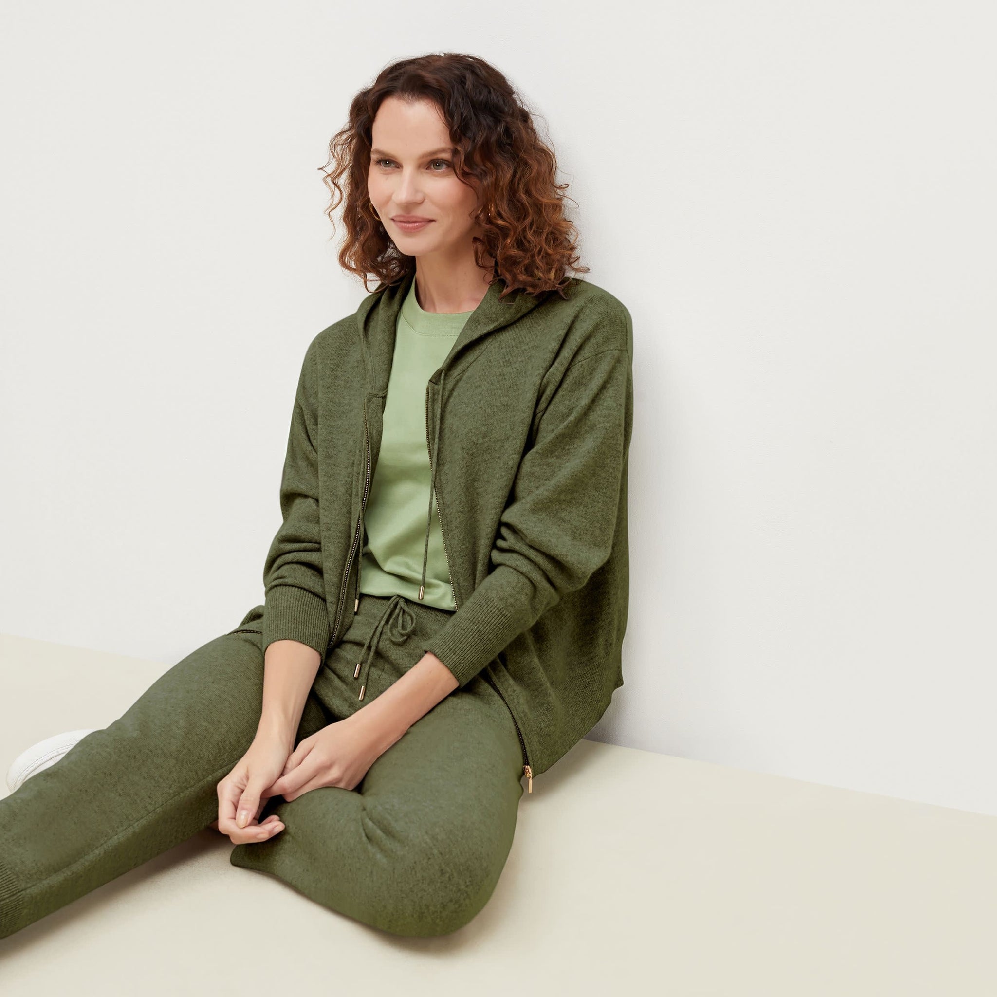 Side image of a woman sitting wearing the Judith Hoodie—Cashmere in Olive